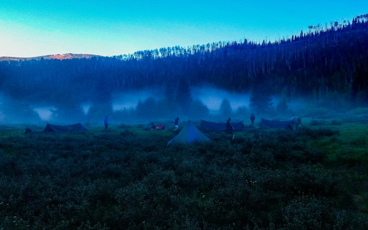 tents and shelters are scattered about a grassy meadow at dawn